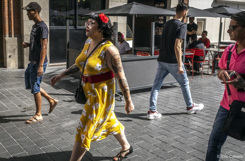 Une jeune femme habillée d'une robe façon années 50 marche dans une rue du centre ville de Toulouse en Occitanie Photojournalisme Streetphotography Eric Cabanis