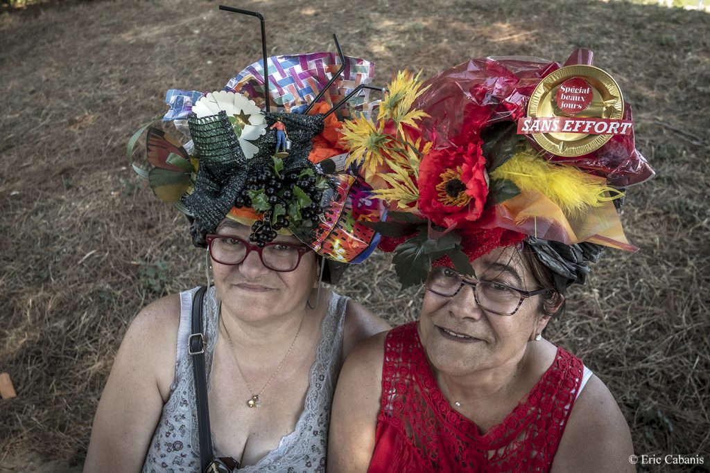 Deux femmes posent avec des chapeaux en papier et carton sur une aire d'autoroute près de Carcassonne en attendant le feu d'artifice du 14 juillet sur la cité médiévale Photojournalisme Streetphotography Eric Cabanis