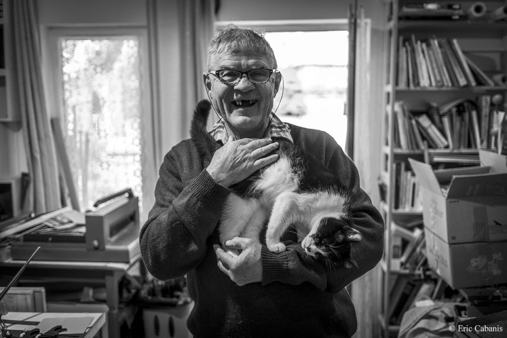 Serge ancien relieur vit aujourd'hui'hui à Rennes les Bains dans la Haute vallée de l'Aude. Il pose avec son chat dans sa bibliothèque le 19 décembre 2019 Photojournalism Streetphotography Eric Cabanis