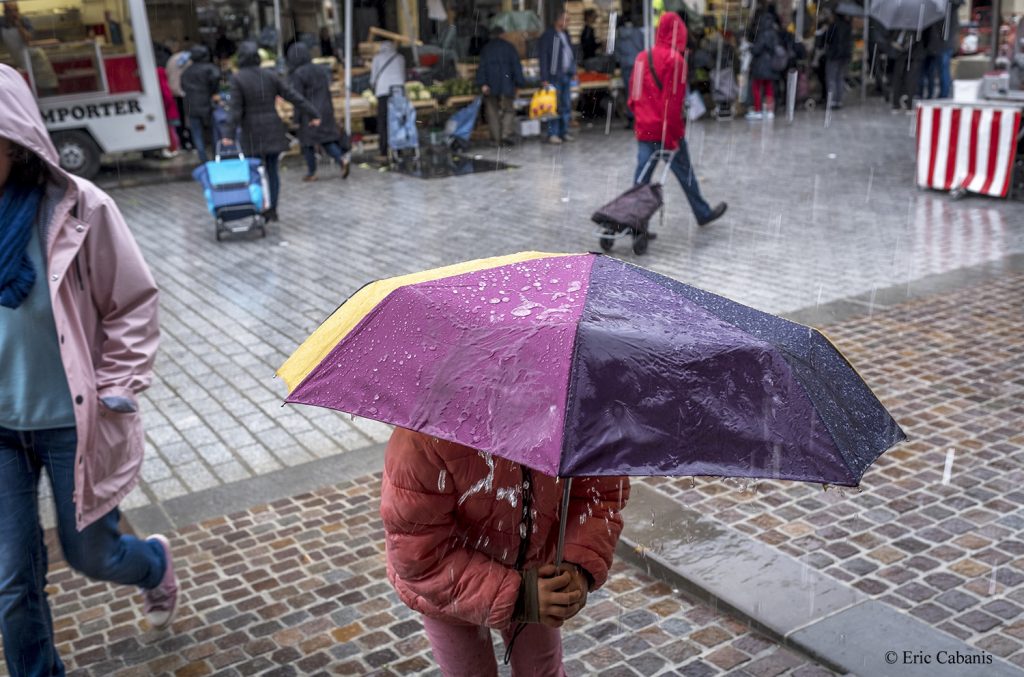 Au marché de Revel en Occitanie une fillette joue sous une averse avec son parapluie Photojournalisme Streetphotography Eric Cabanis