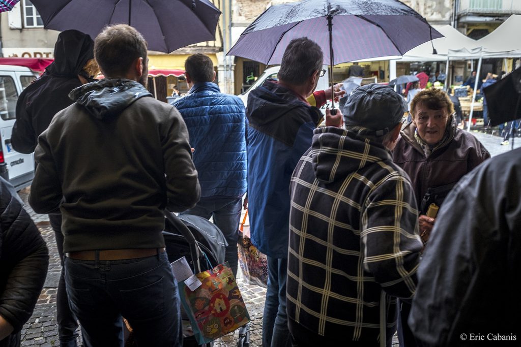 Au marché de Revel en Occitanie des personnes attendent que la pluie cesse de tomber Photojournalisme Streetphotography Eric Cabanis