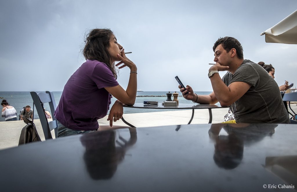 Deux jeunes gens fument une cigarette en attendant d'être servis à la terrasse d'un restaurant à Paphos sur l'île de Chypre en mai 2018 Photojournalism Streetphotography Eric Cabanis