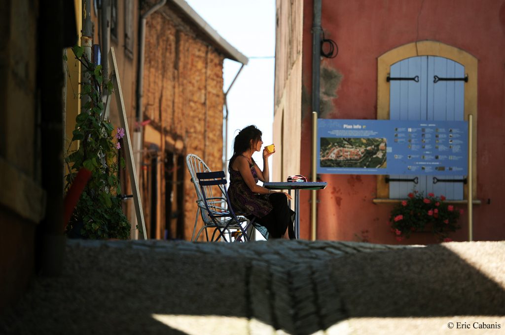 Une fille boit un thé assise sur la place du Carla-Bayle, un village d'artiste en Ariège, en août 2011