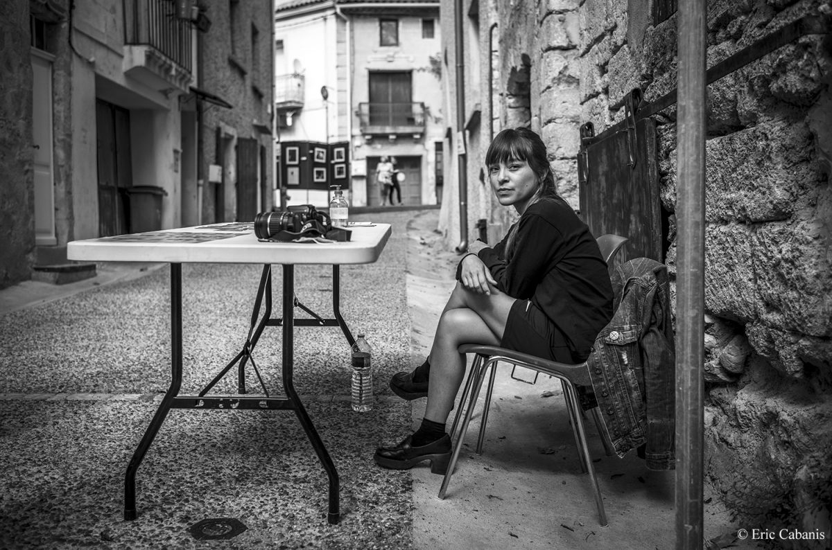 La jeune photographe Thi-Léa Le est assise dans une ruelle de Vendémian où elle expose son travail sur les nuits parisiennes dans le cadre du festival Iso photo festival qui se tient en plein air dans différents sites du village Eric Cabanis Photography